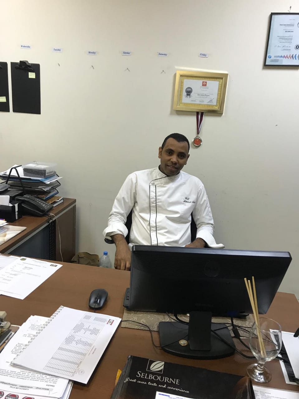 Chef Mohamed Sayed Saleh at his desk, with training certificates and a medal on the wall behind him
