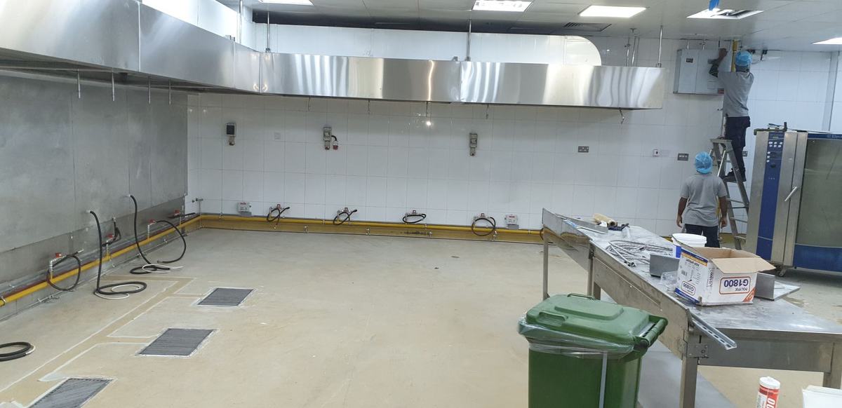 Empty commercial kitchen shell with drainage channels and stainless steel counters
